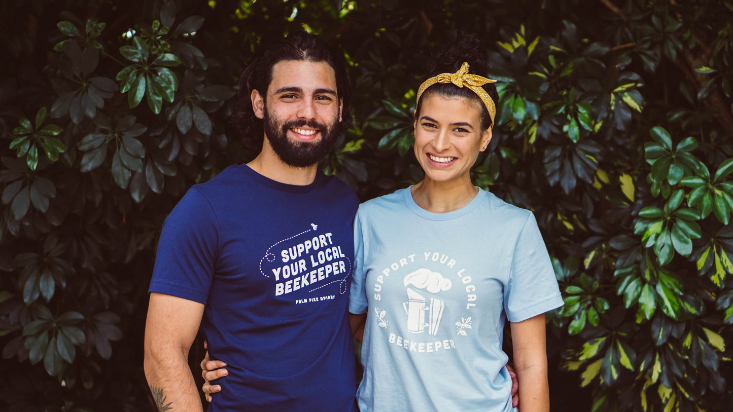 Two people wearing t-shirts with a message about supporting local beekeepers, standing against a leafy green background.